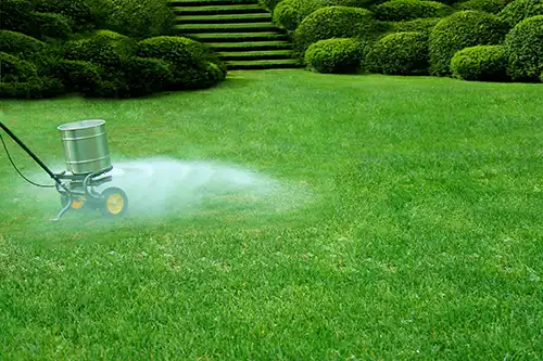Person spreading fertilizer on a lawn - Keep pests away from your lawn with Arrow Exterminators in OK